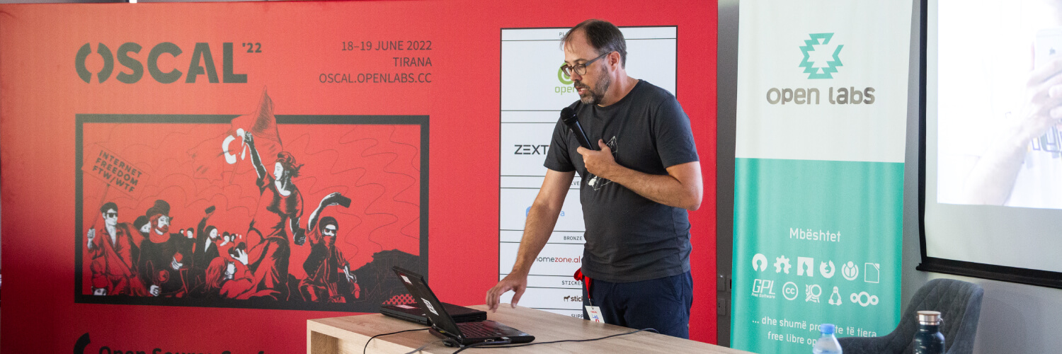 Our dear friend Lars Haefner presenting during OSCAL 2022, with the edition's poster and an Open Labs banner in the background.