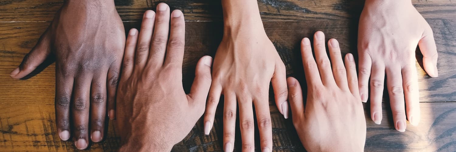 Hands of humans of different colors and genders placed on a table